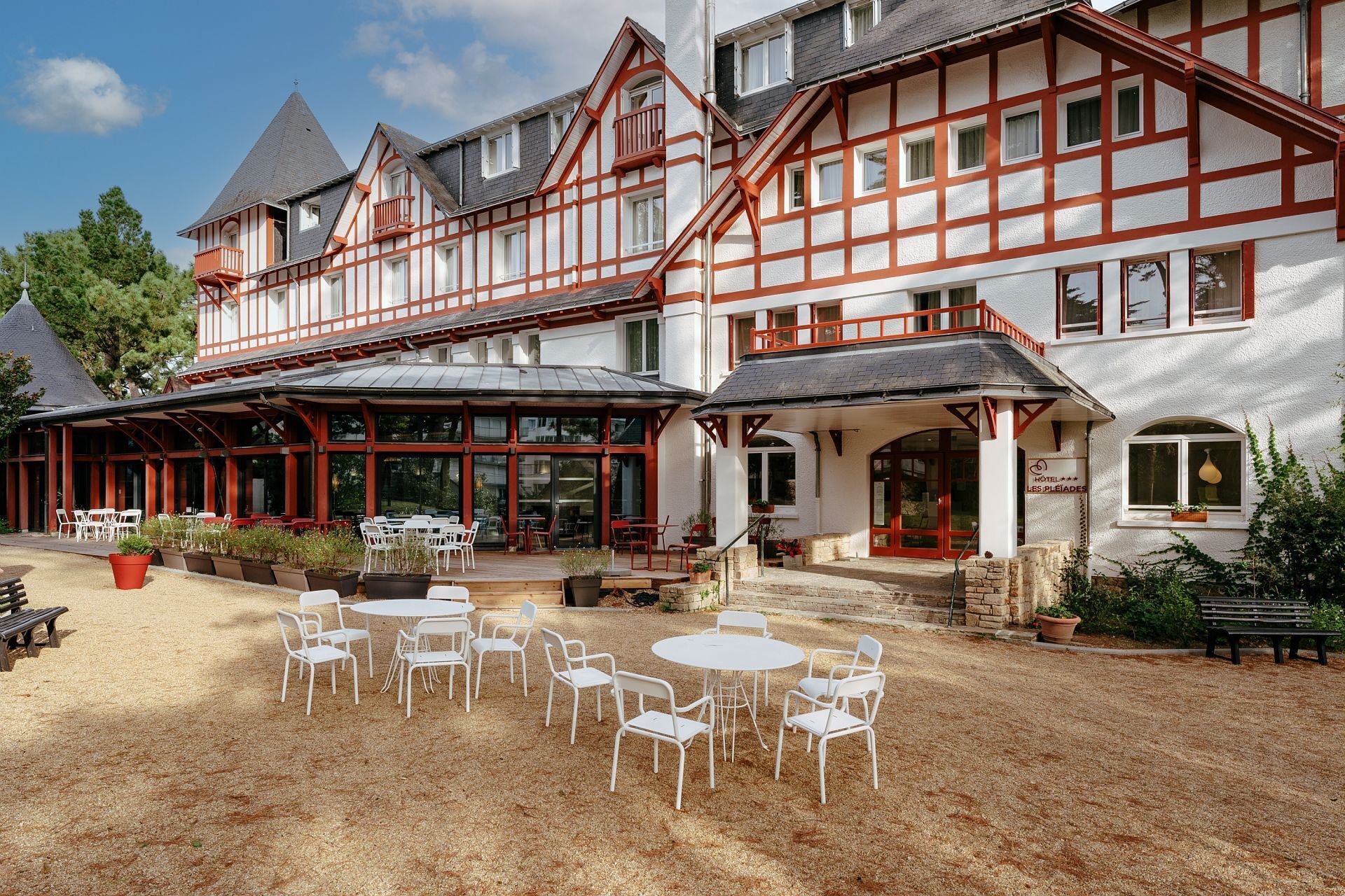 Een traditioneel vakwerkhuis met een overdekt terras, voorzien van witte metalen stoelen en tafels.