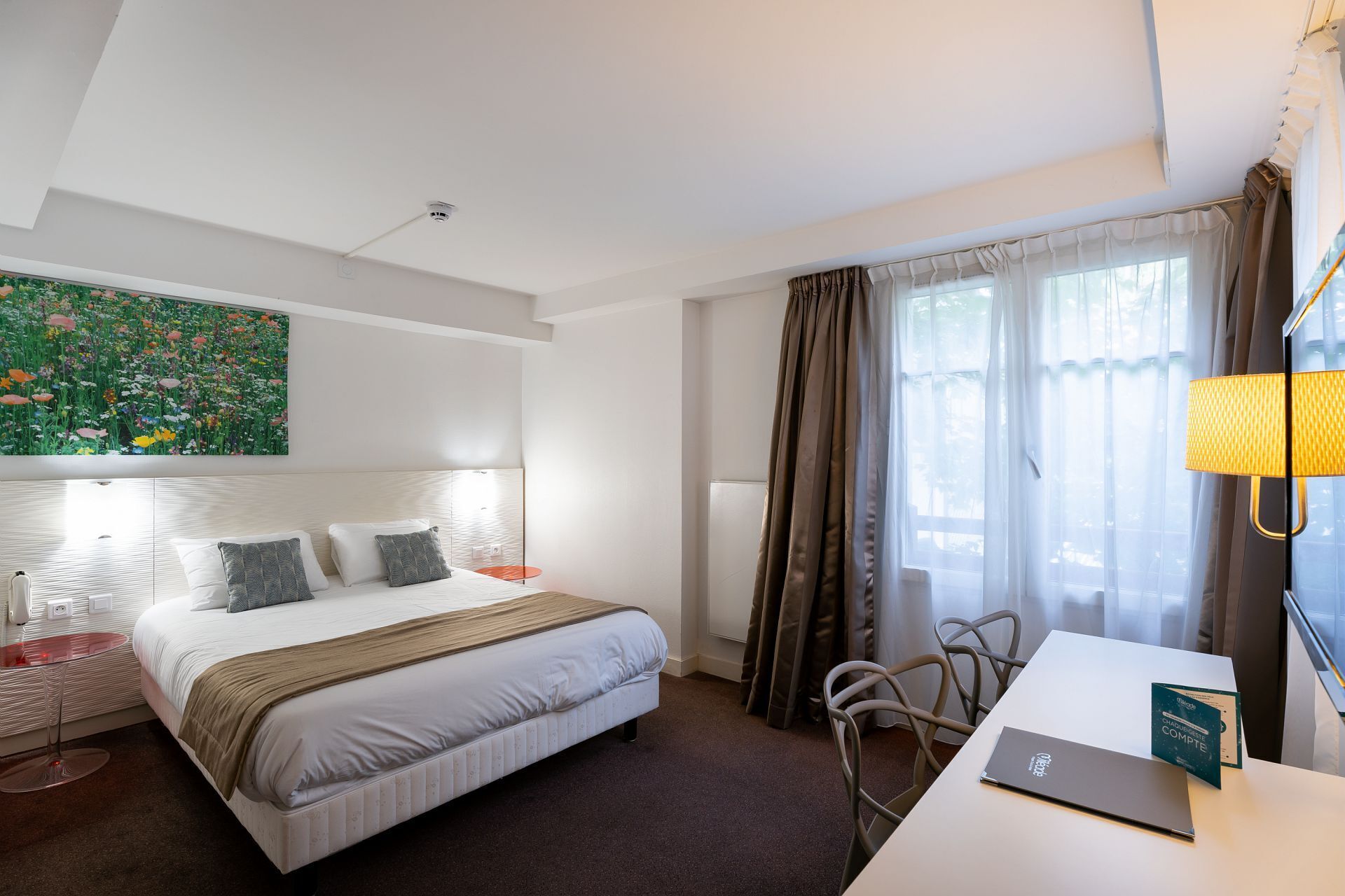 Una habitación de hotel con una cama, un escritorio, una silla, una lámpara y un cuadro en la pared.