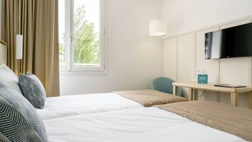 Quarto de hotel com duas camas, uma escrivaninha com cadeira, TV de tela plana e janela com cortinas.