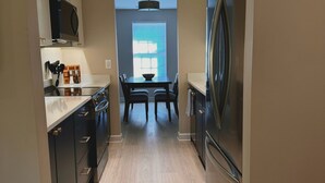 A modern kitchen with dark cabinets, a stainless steel refrigerator, and a dining area with a table and chairs.