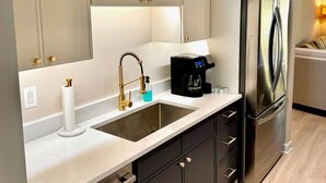 A modern kitchen with a stainless steel refrigerator, a coffee maker, and a sink with a gold faucet.