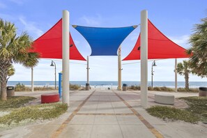 A beachside walkway with a blue canopy, palm trees, and a view of the ocean.
