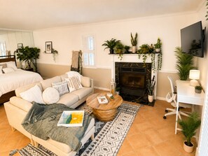 A cozy living room with a sofa, coffee table, and fireplace. There are plants and a TV mounted on the wall.