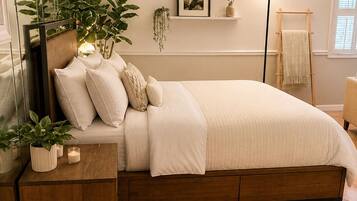 A bedroom with a bed, bedside tables, a mirror, a wall-mounted shelf with plants, a floor lamp, and a window with blinds.