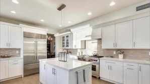 Una cocina moderna con armarios blancos, una isla central, electrodomésticos de acero inoxidable e iluminación empotrada.