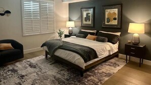 Un dormitorio con cama, mesitas de noche, una silla y ventana con persianas.