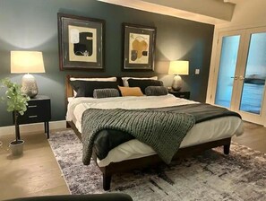 A bedroom with a large bed, two nightstands, a dark wall with two framed pictures, and a door with frosted glass panels. - Lakefront Getaway with Infinity Pool and Pontoon (Glendale)