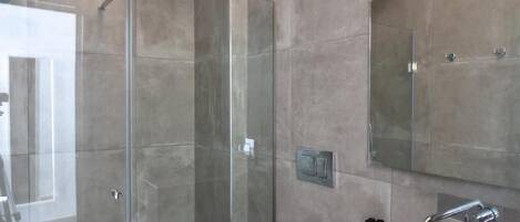 A modern bathroom with a glass shower enclosure, a large mirror, and a sink with a faucet.