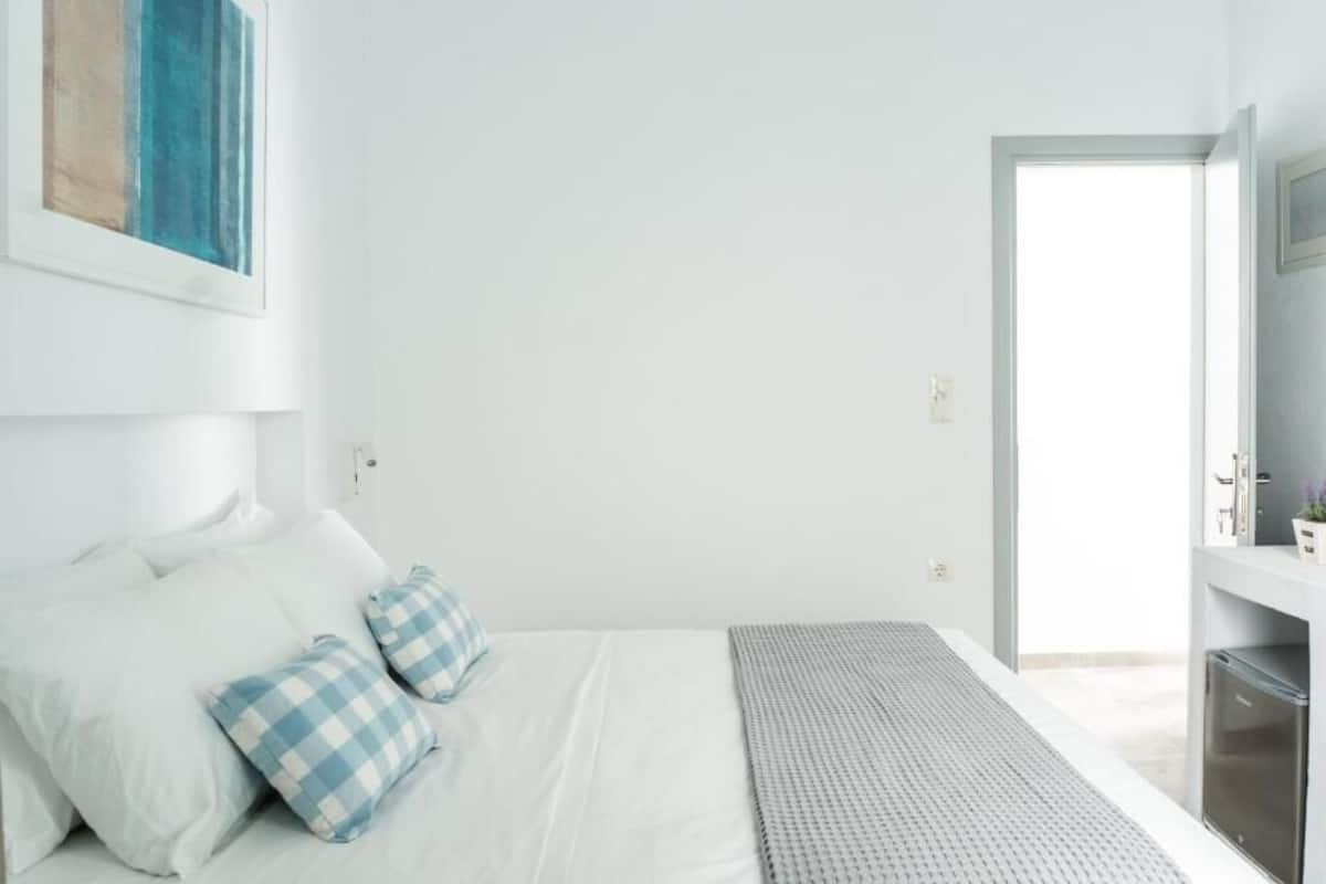 A bedroom with a bed, pillows, a bedside table, and a door leading to a bathroom.