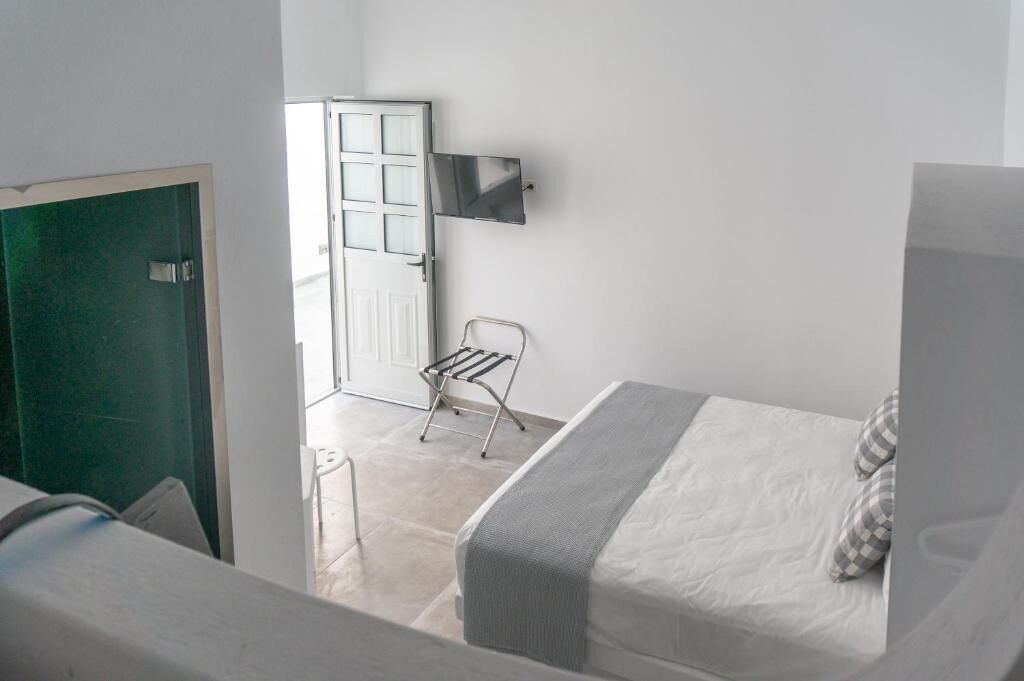 A small, compact room with two beds, a wall-mounted TV, and a door leading to another room.