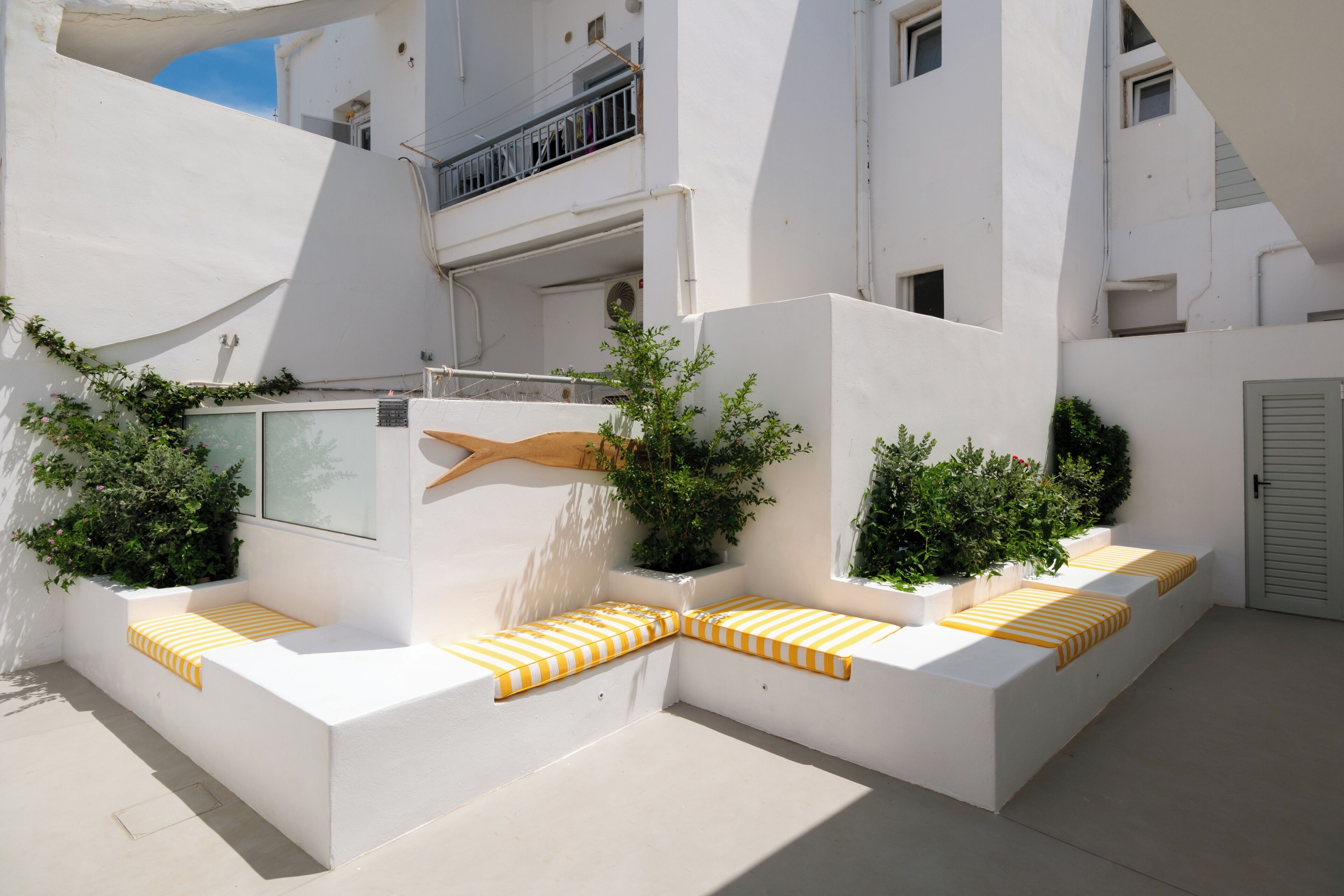 A modern outdoor seating area with built-in benches and planters, surrounded by white walls and balconies.