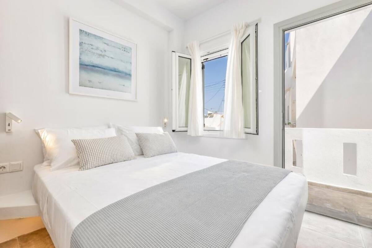 A bedroom with a bed, a window with curtains, a painting on the wall, and a balcony.