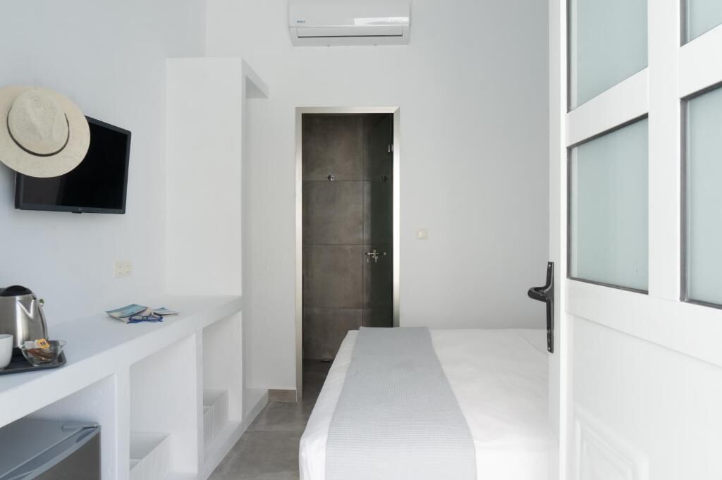 Une chambre d’hôtel moderne équipée d’un lit, d’un téléviseur fixé au mur, d’une petite table avec une machine à café et d’une porte donnant sur une autre pièce.