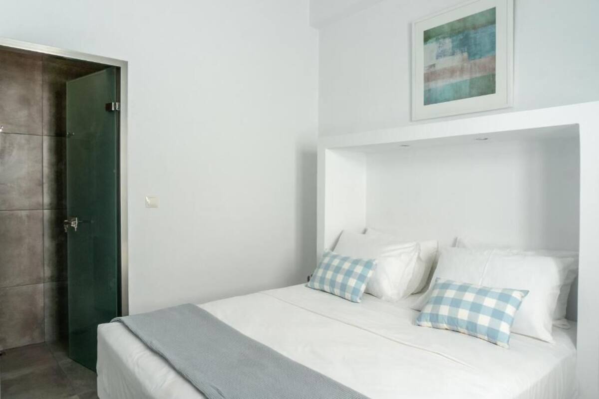 A bedroom with a bed, a checkered pillow, a grey blanket, a framed picture on the wall, and a green door.
