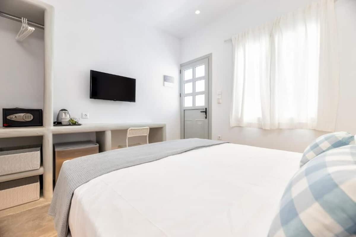 A bedroom with a bed, a desk, a chair, a television, and a window with curtains.