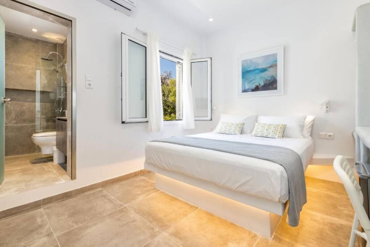 A bedroom with a bed, a shower, and a window with curtains.