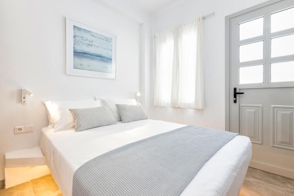 Une chambre à coucher avec un lit, une fenêtre avec des rideaux, une porte et un luminaire fixé au mur.