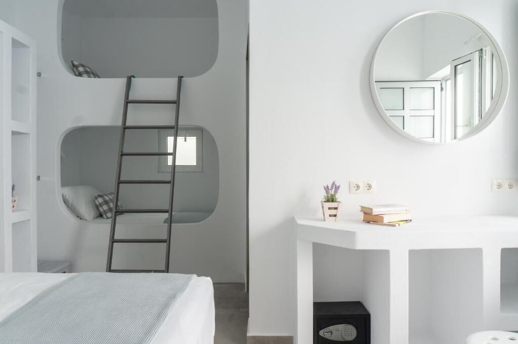 Un dormitorio con literas, una escalera, una mesita de noche con espejo y un escritorio pequeño con una planta y libros.