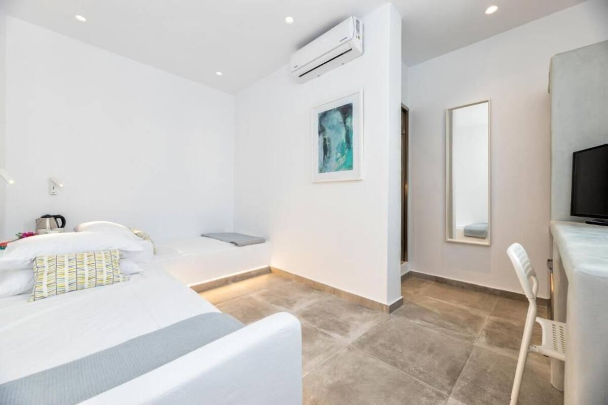 A modern hotel room with a bed, a chair, a desk, an air conditioner, a painting, and a mirror.