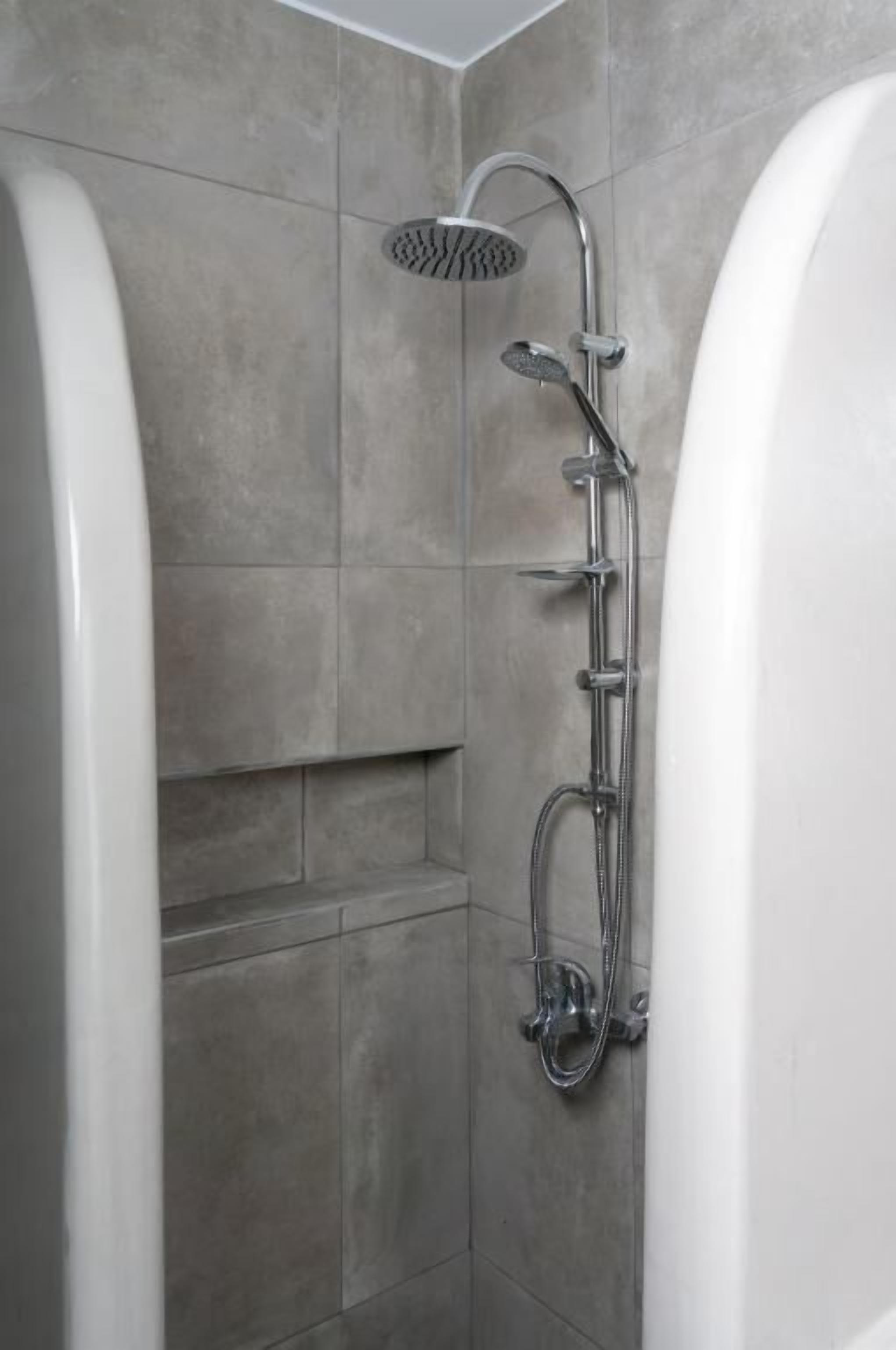 A modern bathroom with a walk-in shower, a bathtub, and grey tiled walls.