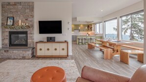 Una sala de estar moderna con chimenea de piedra, un televisor de pantalla plana y una mesa de comedor de madera con bancos.