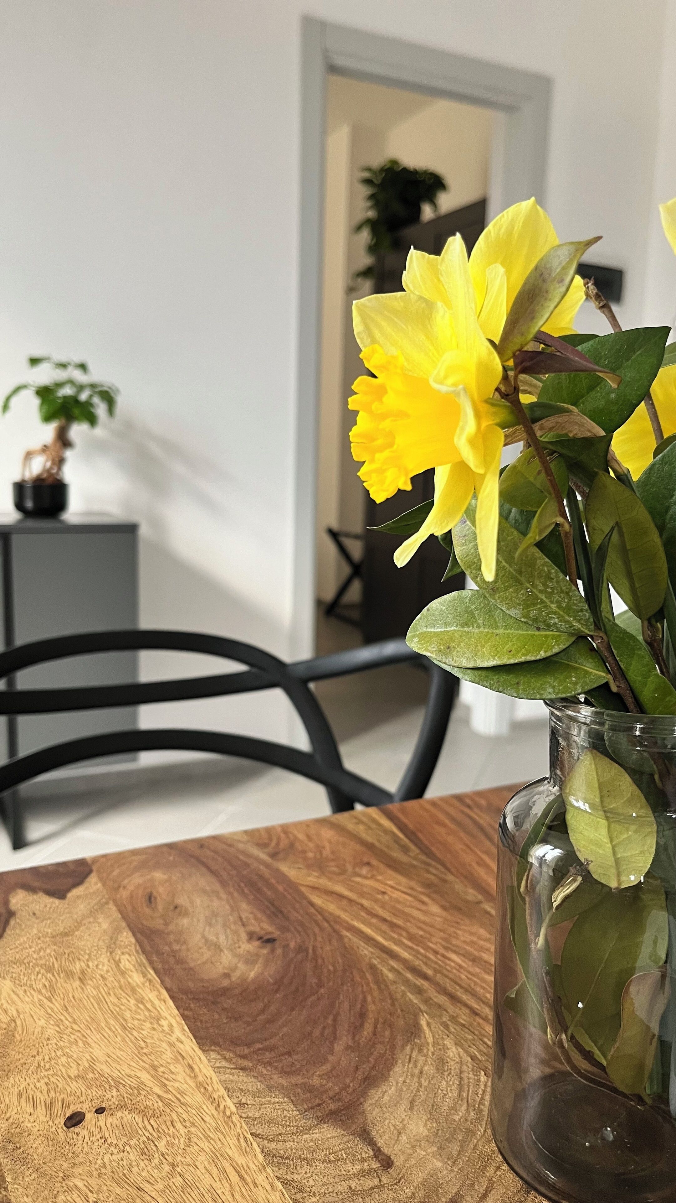 A wooden table with a glass vase containing yellow flowers.