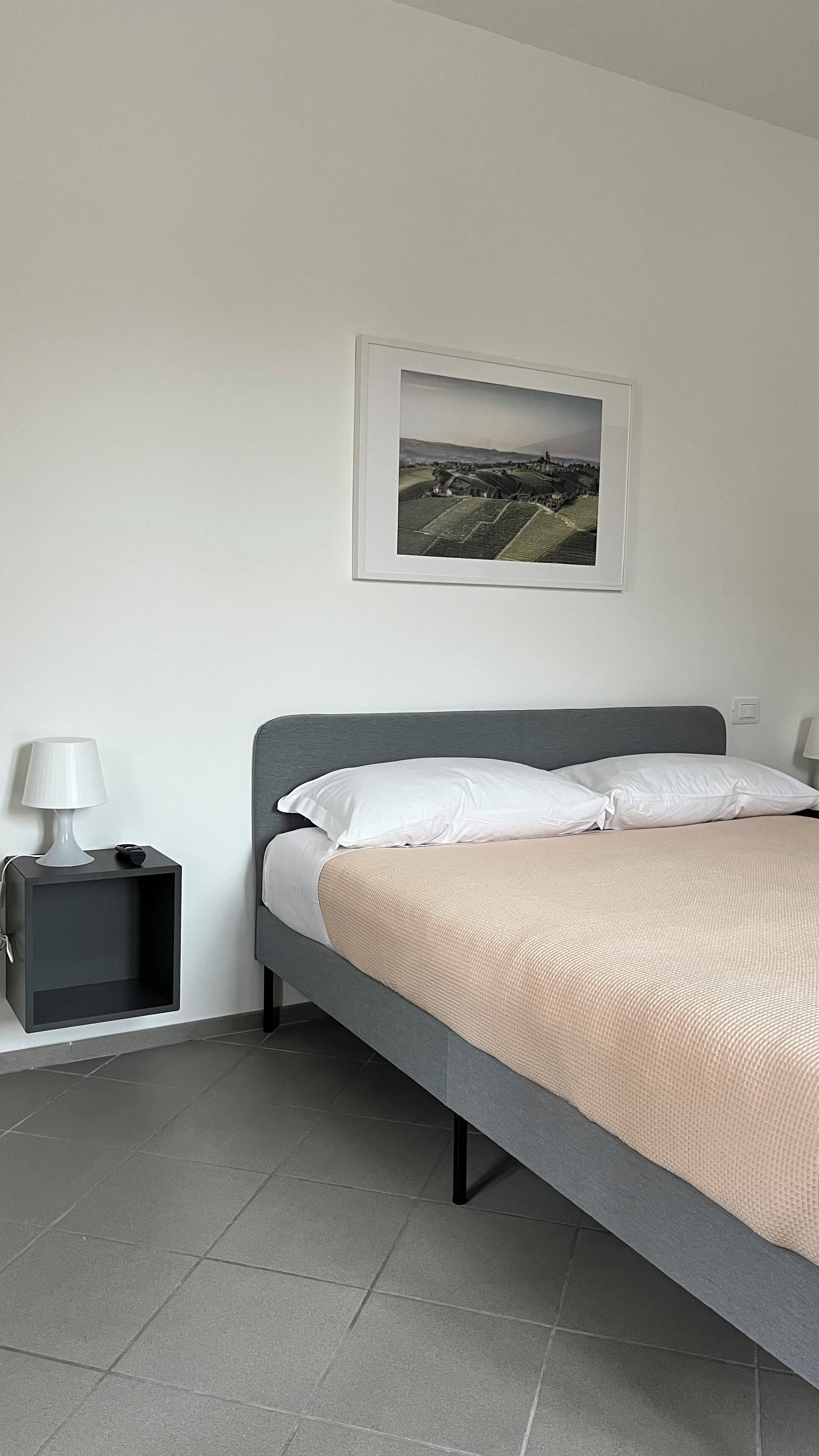A bedroom with a bed, a nightstand, a lamp, and a framed picture on the wall.