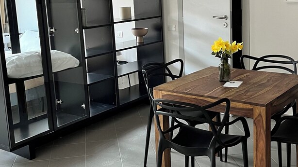 Un comedor moderno con una mesa y sillas de madera, un jarrón de flores y un mueble negro con puertas de cristal.