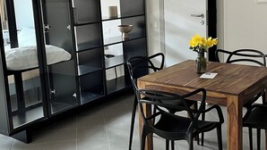 Un comedor moderno con una mesa y sillas de madera, un jarrón de flores y un mueble negro con puertas de cristal.