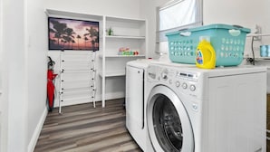 A laundry room with a washing machine, a drying rack, a shelf with toys, a basket, and a bottle of detergent. - Perfect Location for Sports and Concert Venues! - La Cabina (Tampa)