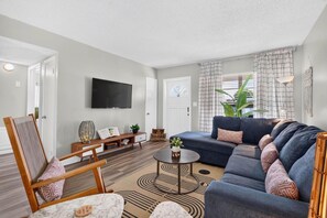 Ein modernes Wohnzimmer mit Sofa, Sessel, Couchtisch und einem wandmontierten Flachbildfernseher.