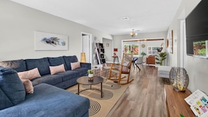 A modern living room with a sofa, coffee table, and a rocking chair. There is a dining area with a table and chairs in the background. - Perfect Location for Sports and Concert Venues! - La Cabina (Tampa)
