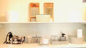 A kitchen with white cabinets, a floral-patterned iron, a white basket, and a white tray with glassware. - The Gardenia Suites in The Heart of Spring Hill-A (Spring Hill)