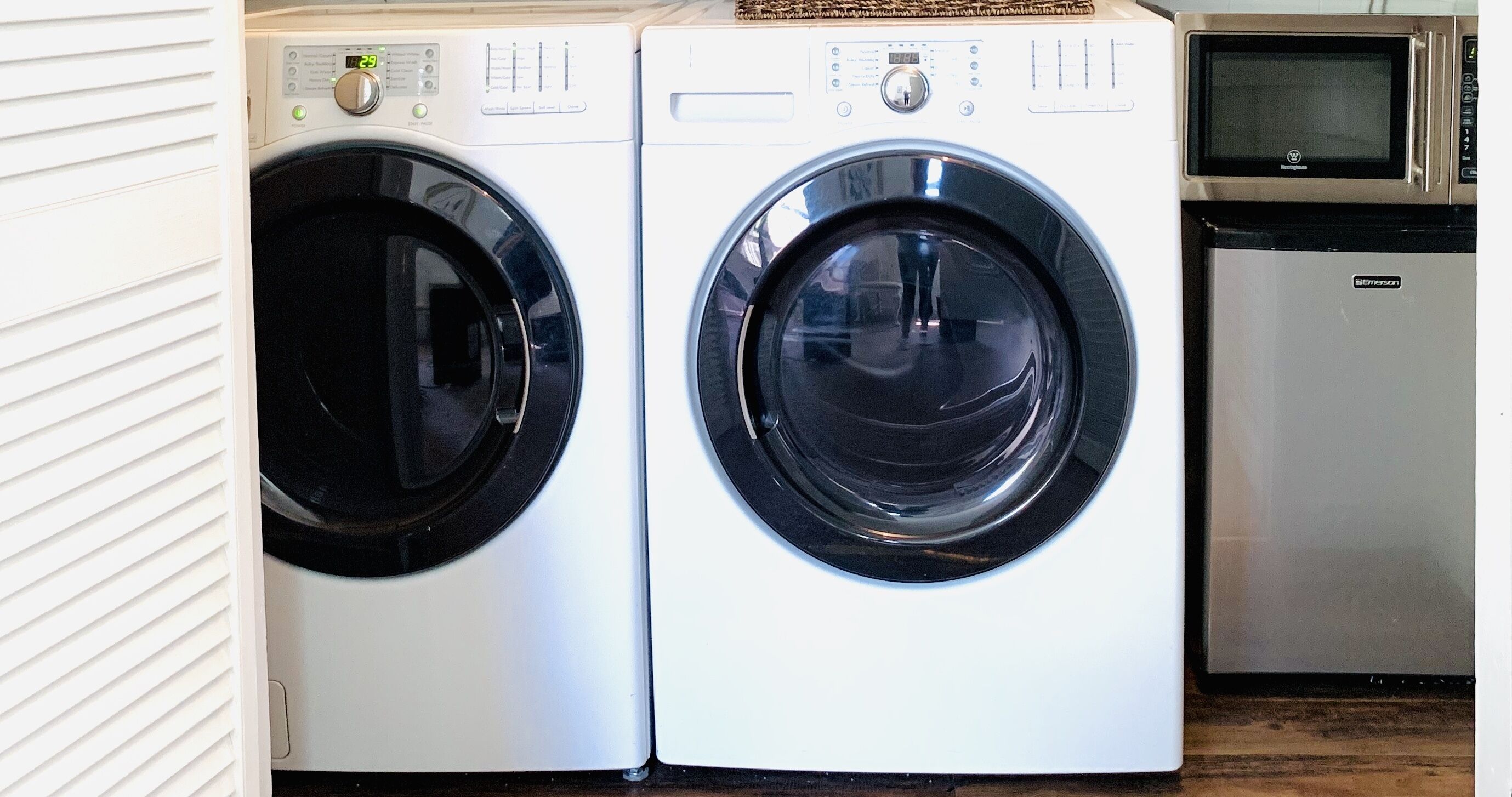 A front-loading washer and dryer unit with a digital display, control panel, and a microwave above it.