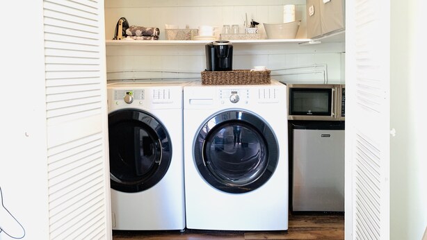 A compact laundry room with two front-loading washing machines, a coffee maker, and a microwave on the countertop. - The Gardenia Suites in The Heart of Spring Hill-A (Spring Hill)