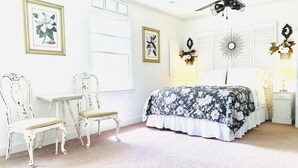 A bedroom with a bed, two chairs, a ceiling fan, and decorative wall art. - The Gardenia Suites in The Heart of Spring Hill-A (Spring Hill)