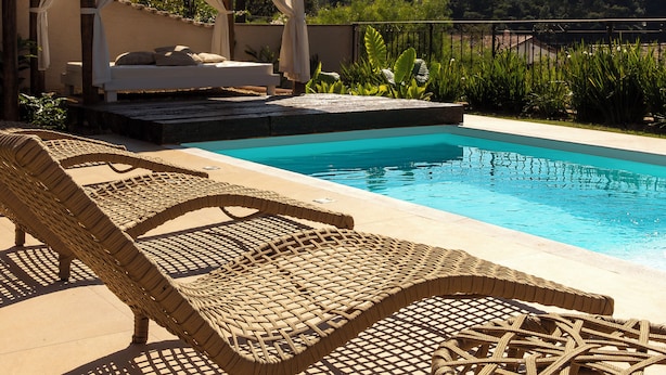 A poolside area with a bed under a canopy, wicker lounge chairs, and a view of a mountain. - Villa Boréal Hostellerie (Águas de Lindóia)