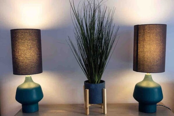 Two lamps with dark shades and blue bases, a potted plant in the center, and a wooden stand. - Beautiful seaside retreat close to North Devon's white sandy beaches! (Wrafton)