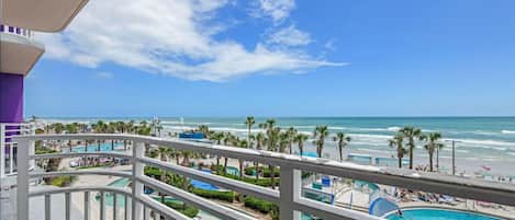 A balcony with a view of a beach, a pool area, and a clear sky.