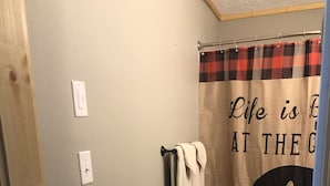 A bathroom with a wooden floor, a towel rack with a white towel, a shower curtain with a bear silhouette and text, and a light switch on the wall.