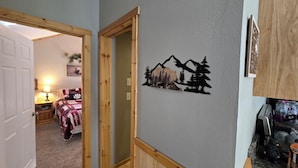 A bedroom with a bed, a nightstand, and a lamp. There is a wooden door frame and a wall decoration of mountains and trees.