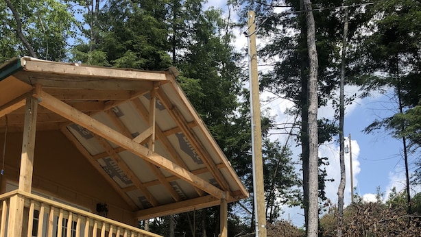 A wooden cabin with a balcony, surrounded by trees and a dirt path leading up to it.