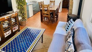A living room with a sofa, a coffee table, and a TV. There is a dining area with a table and chairs. - Townhouse in the vibrant old town (Tarifa)
