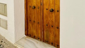 A wooden double door with metal studs and a small square window, set in a white wall with a number '6' sign above. - Townhouse in the vibrant old town (Tarifa)