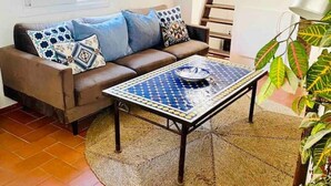 A living room with a brown leather sofa, patterned cushions, a blue and yellow tiled coffee table, a woven rug, and a staircase leading to an upper level. - Townhouse in the vibrant old town (Tarifa)