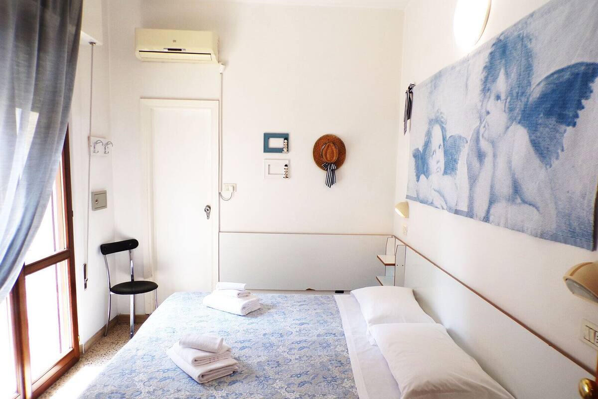 A hotel room with a bed, a chair, a painting, and a door.