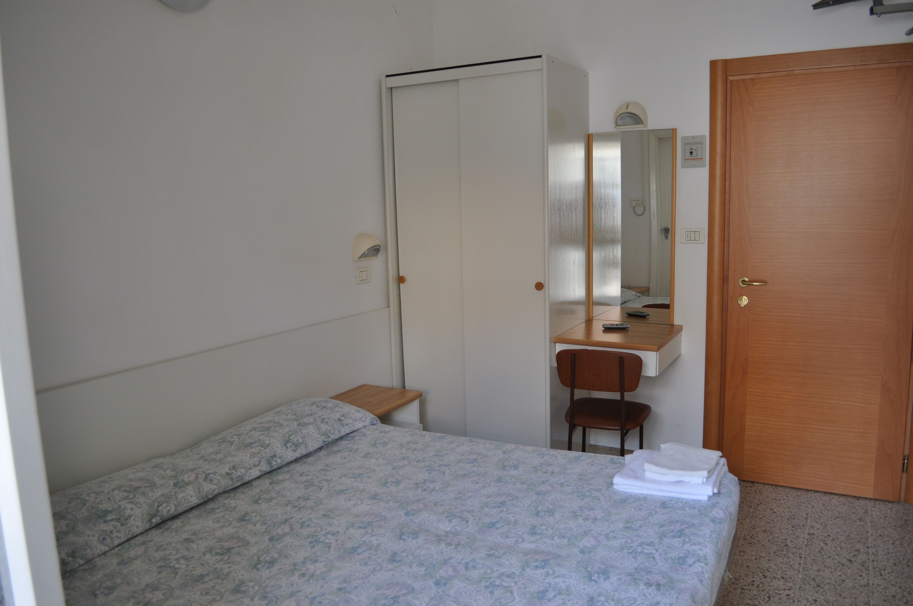 Ein Schlafzimmer mit Bett, Schreibtisch, Stuhl, Kleiderschrank und einer Tür.