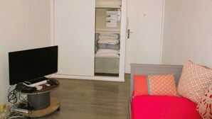 A room with a TV on a stand, a wardrobe with hanging clothes, and a bed with patterned pillows. - Limoges,,belle vue ! (Limoges)