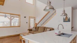 A spacious living area with a large island, wooden flooring, a staircase, and a view of the outdoors. - Discover Lake Granby steps away (Granby)