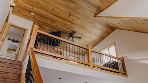 A spacious loft with a high ceiling, wooden beams, a balcony with a railing, and a staircase leading to an upper level. - Discover Lake Granby steps away (Granby)